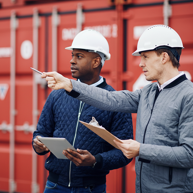 Two men in hard hats holding clipboards and pointing off into the distance