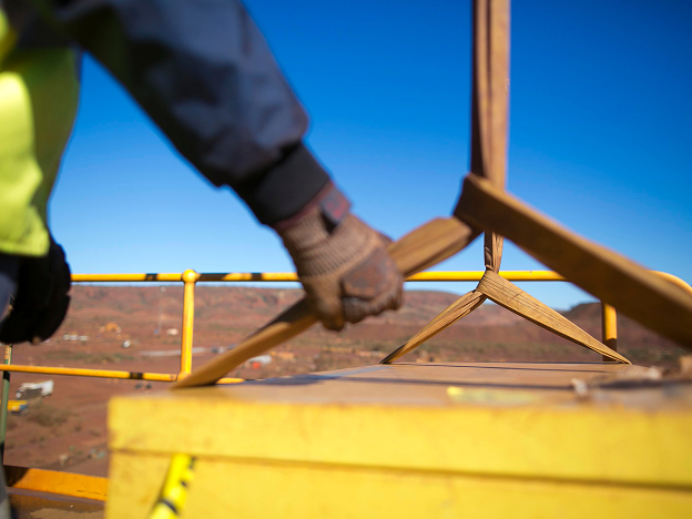 A man wearing a safety vest and gloves outdoors holding a rope that's hoisting a large container