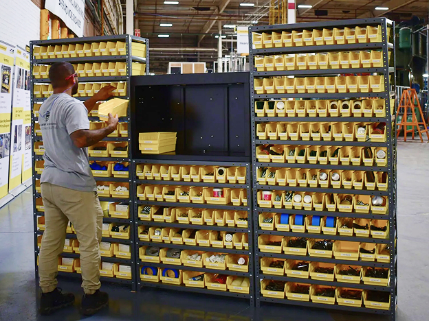 A man in a warehouse sorting tools at a large shelf